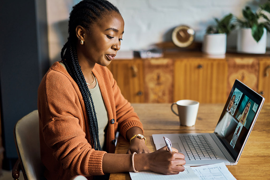 Woman sitting at a laptop taking notes in a notebook